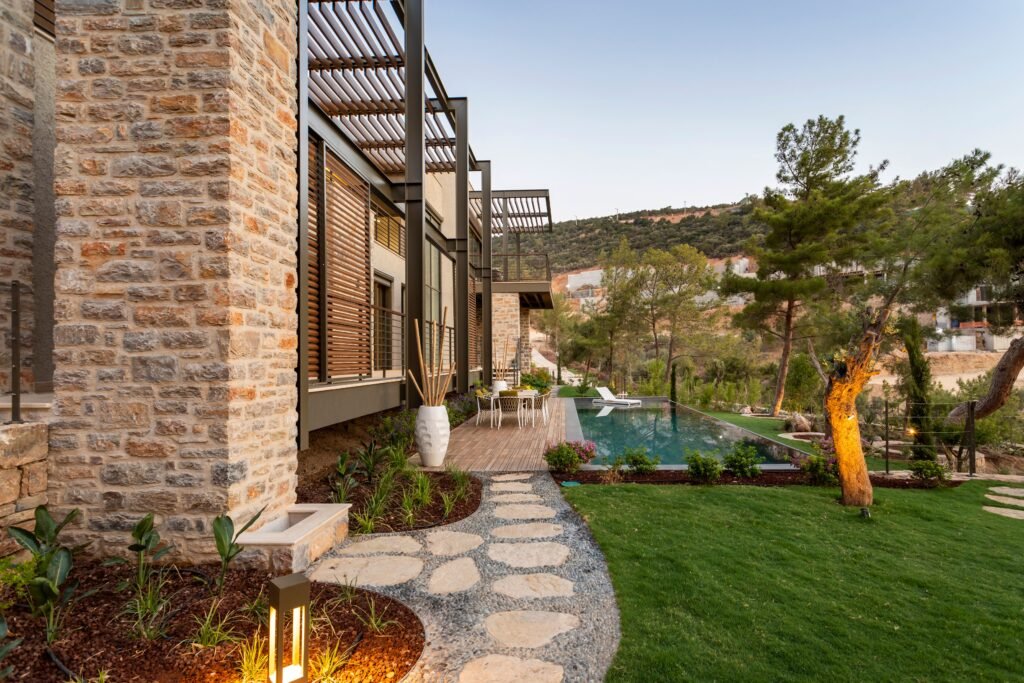 Modern villa in Bodrum featuring a stone facade, lush garden, and infinity pool with scenic views.