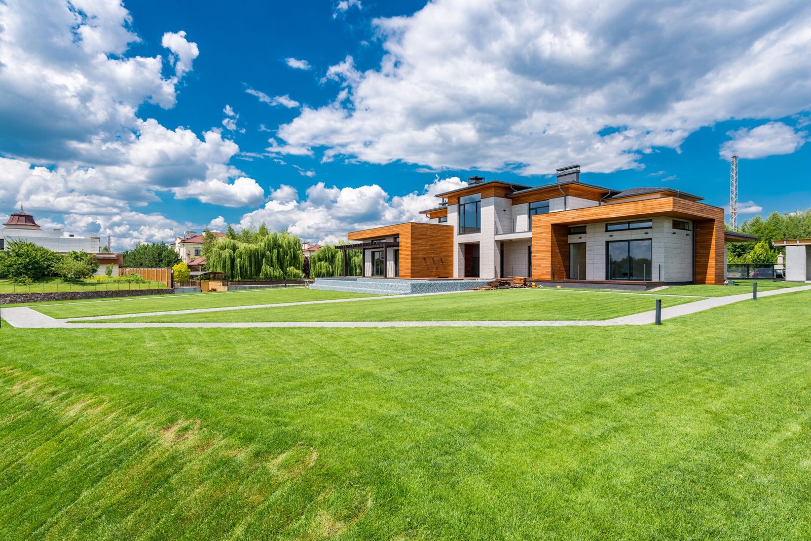 Exterior of modern residential house with wooden walls and green grass growing in yard against blue sky with white clouds